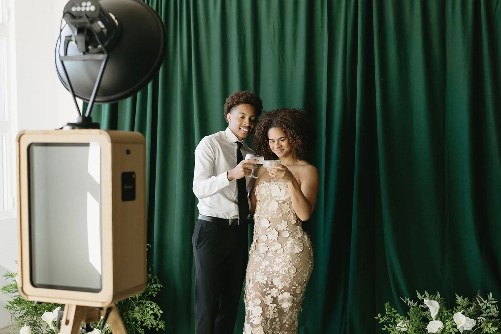 A couple pose in front of a green backdrop for their Studio Photo Booth portrait to be captured.